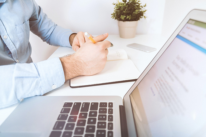 man sitting next to a computer taking notes